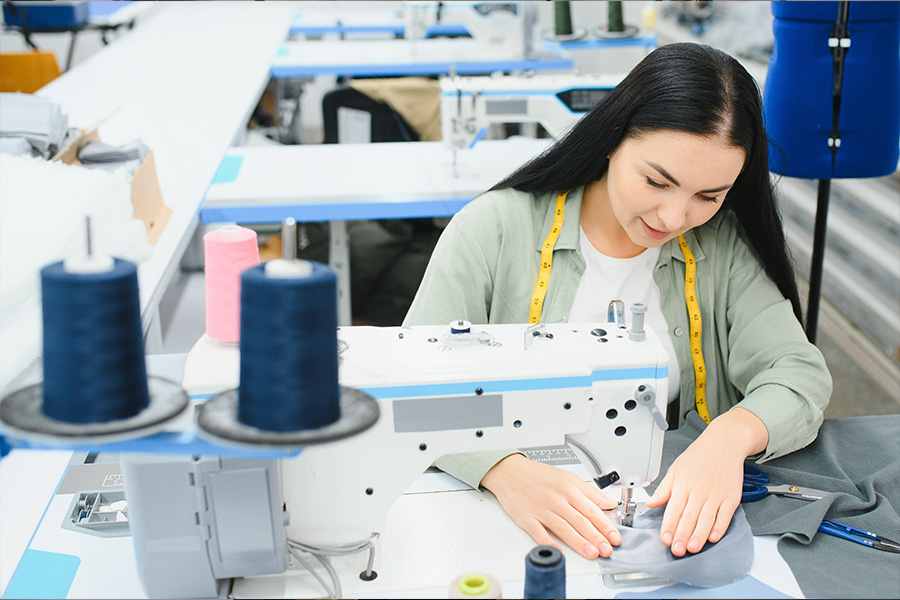 A woman using a sewing machine with spools of thread in the foreground and fabric in her hands.