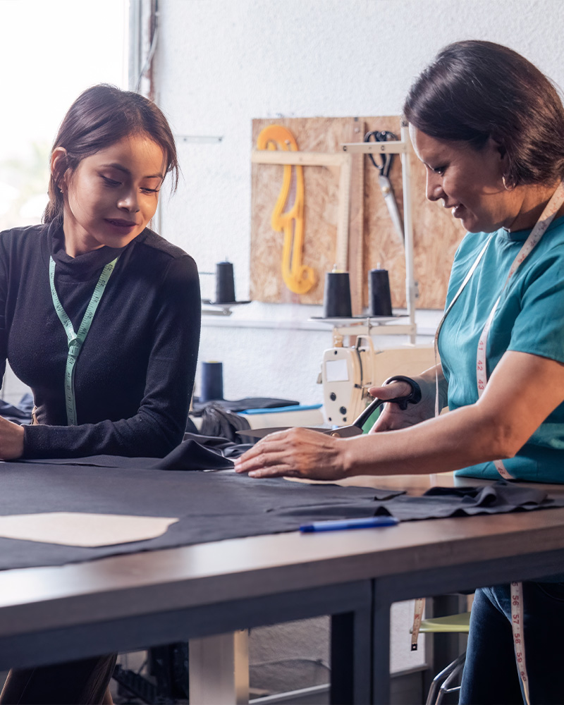 Two women collaborating on fabric sewing at a work table in a sewing studio.